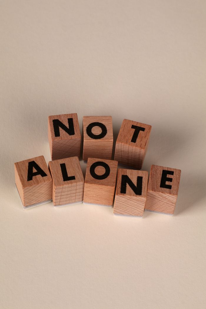 Encouragement concept with wooden blocks spelling 'Not Alone' on a neutral background.